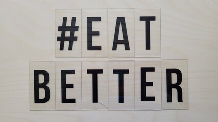 Hashtag # Eat Better with black letters on beige wooden background, logo design, label, notes, positive quote. Poster for advertising, text art. Label on wall.