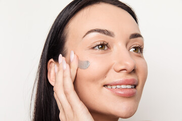 Young caucasian brunette woman applying grey cream on her face 