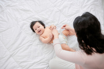 Mother changing her baby's diaper on bed