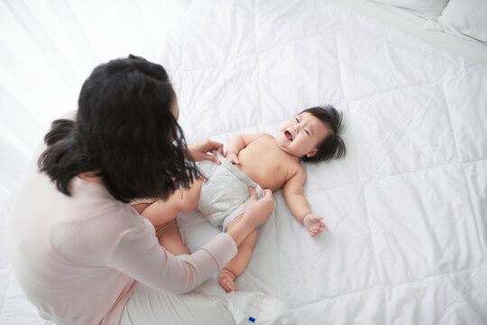 Mom changing diaper for her little girl on bed