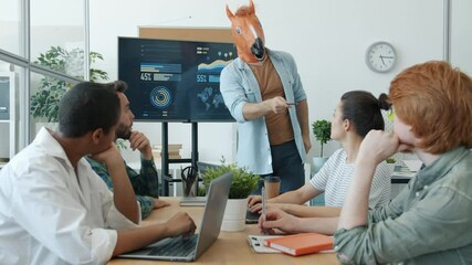 Businessman wearing horse head mask is making presentation in office to group of employees speaking and pointing at digital screen. Crazy business and modern technology concept. - Powered by Adobe
