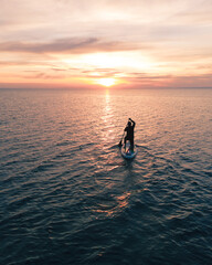 silhouette of a surfer with a paddle sailing in the sun during sunset