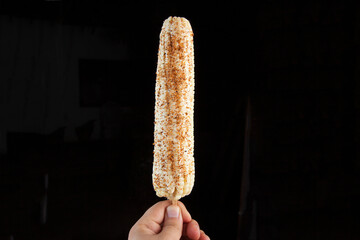 mexican boiled white corn on the cob with chili, lime and mayonnaise on black background