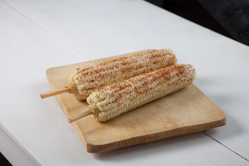 mexican boiled white corn on the cob with chili, lime and mayonnaise on wooden table 