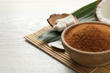 Natural coconut sugar in bowl on white wooden table, space for text