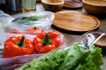 cucumbers, tomatoes, bell peppers and lettuce in bags on the kitchen table. 