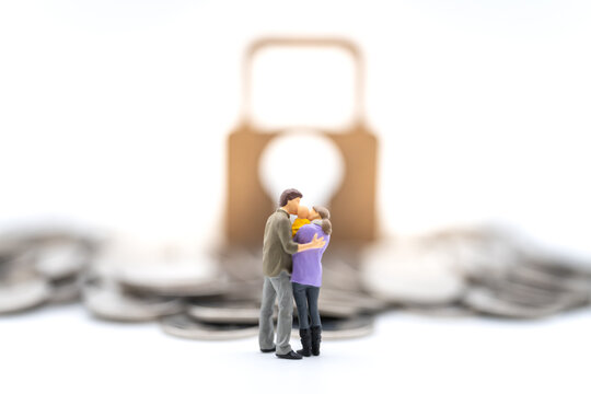 Money, Financial, Business Security and Family concept. Parent and child miniature figures hug and kiss together standing with pile of coins and master key lock icon on white background.