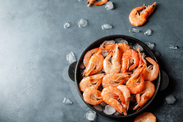 Raw shrimps with ice cubes on grey background. Uncooked shrimps