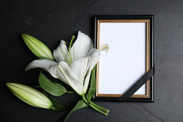 Funeral photo frame with ribbon and white lily on black table, flat lay. Space for design - obrazy, fototapety, plakaty