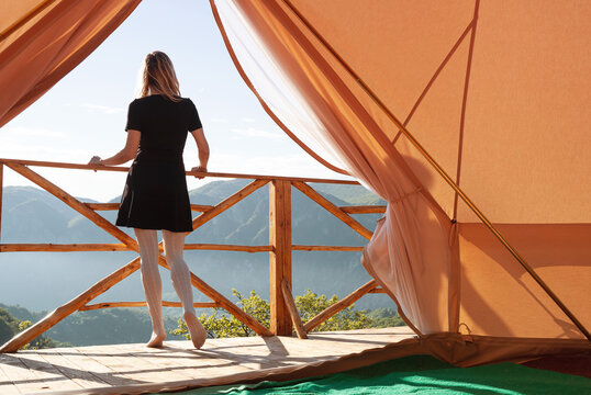 young woman watching the mountains in front of a glamping tent - Powered by Adobe