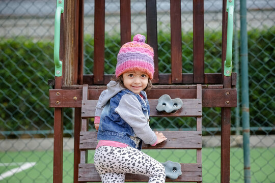 Crian&ccedil;a linda brincando num parquinho de touca rosa e blusa azul no inverno depois da quarentena do covid 19.