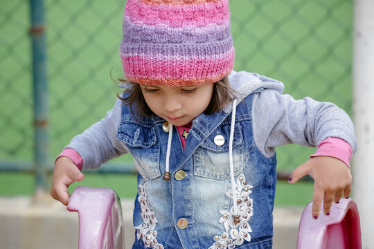 Crian&ccedil;a linda brincando num parquinho de touca rosa e blusa azul no inverno depois da quarentena do covid 19.