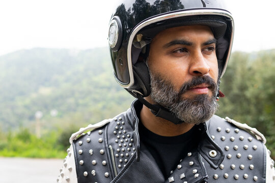 Self esteem ethnic male biker in helmet standing on road and looking away