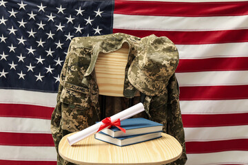 Diploma, books and soldier uniform on wooden chair near flag of United States. Military education