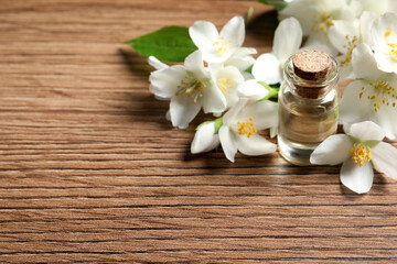 Fototapeta na wymiar Jasmine essential oil and fresh flowers on wooden table, space for text