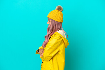 Young woman with pink hair wearing a rainproof coat isolated on blue background in lateral position