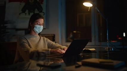 Female Manager in Protective Face Mask Works on Laptop Computer in Creative Agency in Loft Office in the Evening. Specialist Calmly Looks at Camera. Renovated Stylish Design with House Plants. - Powered by Adobe