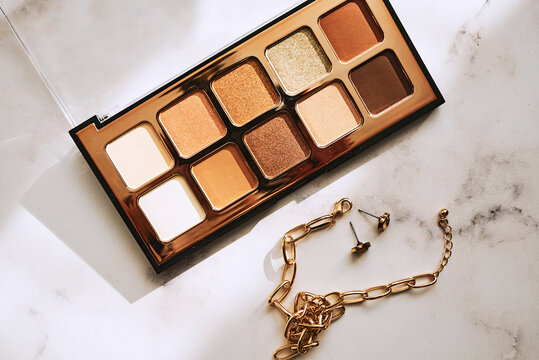 Colorful cosmetic eyeshadow palette makeup set with golden tint and gold bracelet on marble background.