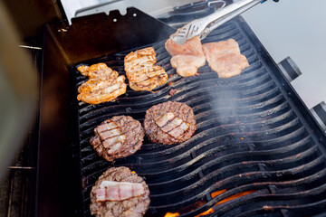 Cook grills burger patties and pork ribs open fire. Turns meat over with tongs