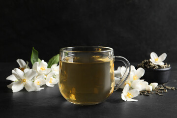 Glass cup of jasmine tea and fresh flowers on black table - obrazy, fototapety, plakaty
