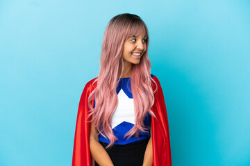 Young superhero woman with pink hair isolated on blue background looking side