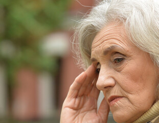 sad senior woman  with headache in  park