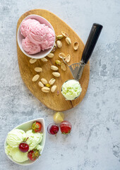 Bowl and scoops with delicious raspberry, cherry and pistachio ice cream.Wooden plate with delicious ice cream and different ingredients on the table decorated with branches and flowers.