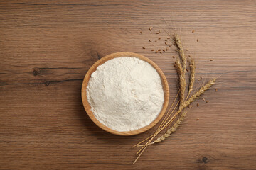 Bowl of flour and wheat ears on wooden table, flat lay