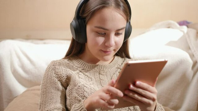 Portrait of smiling teenage girl with headphones using tablet computer and browsing internet