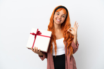 Young woman with orange hair holding a gift isolated on white background showing ok sign with fingers