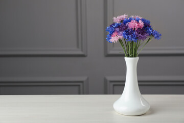 Bouquet of beautiful cornflowers in vase on white wooden table. Space for text