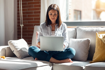 Pretty young woman working with her laptop while sitting on couch at home.