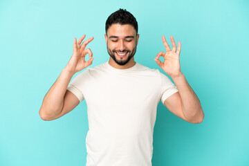 Young arab man isolated on blue background in zen pose