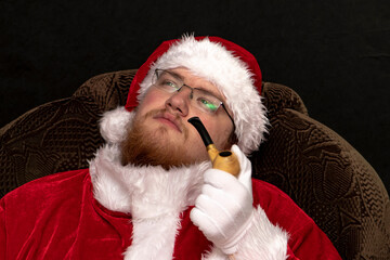 Portrait of a resting Santa Claus with a pipe and a beard on a dark background.