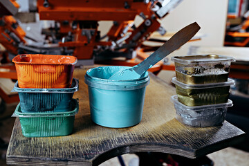 selective focus photo of various paints on wooden shelve on the print screening apparatus. serigraphy production. printing images on t-shirts