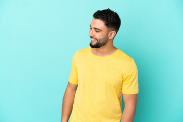 Young arab man isolated on blue background looking to the side and smiling