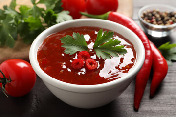 Spicy chili sauce with parsley on wooden table, closeup