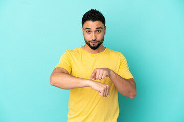 Young arab man isolated on blue background making the gesture of being late