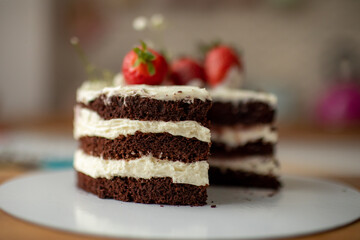 A pastry chef holds a chocolate cream cake on a stand, decorated with strawberries.