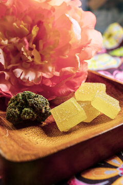 Close up of cannabis bud and infused gummies with a flower in the background.