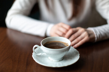 coffee in a beautiful openwork cup and saucer on the table in front of a girl in a light jacket