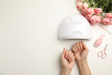 Woman doing manicure with ultraviolet nail lamp at white table, top view. Space for text
