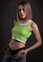 Gorgeous sexy blonde girl in a crop top and jeans poses on a dark background