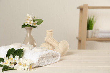 Beautiful jasmine flowers, towel, spa stones and herbal bags on white wooden table indoors, space for text