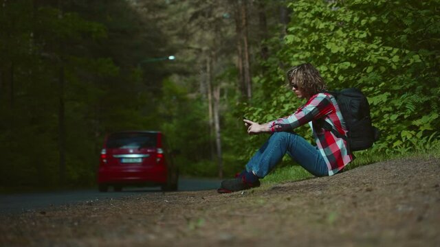 Male tourist sitting near the road with mobile phone.