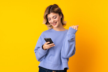 Young Russian woman isolated on yellow background with phone in victory position