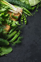 Fresh vegetables and wooden cutting board on a black textured background.