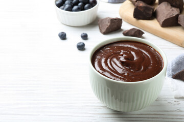 Delicious chocolate cream and blueberries on white wooden table, space for text