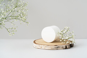 Plastic jar on wooden tray and flowers on grey background. White round cosmetic container for...
