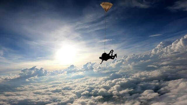Tandem skydiving in a dramatic sky. The sun illuminates the clouds at the end of the day. Slow motion movie.